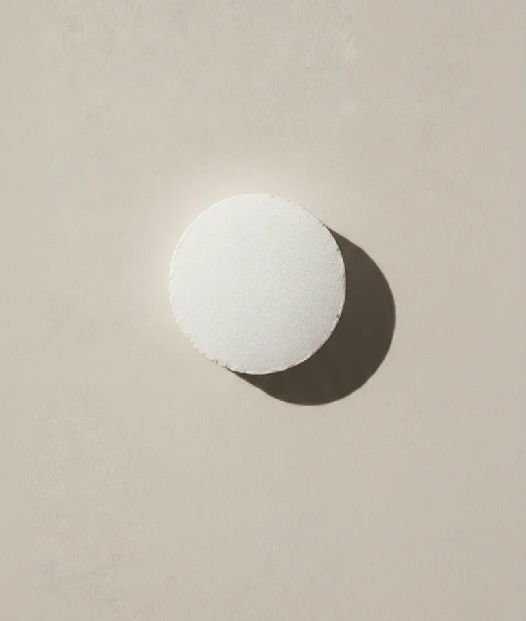 White Faeora toothpaste tablet on a beige background.