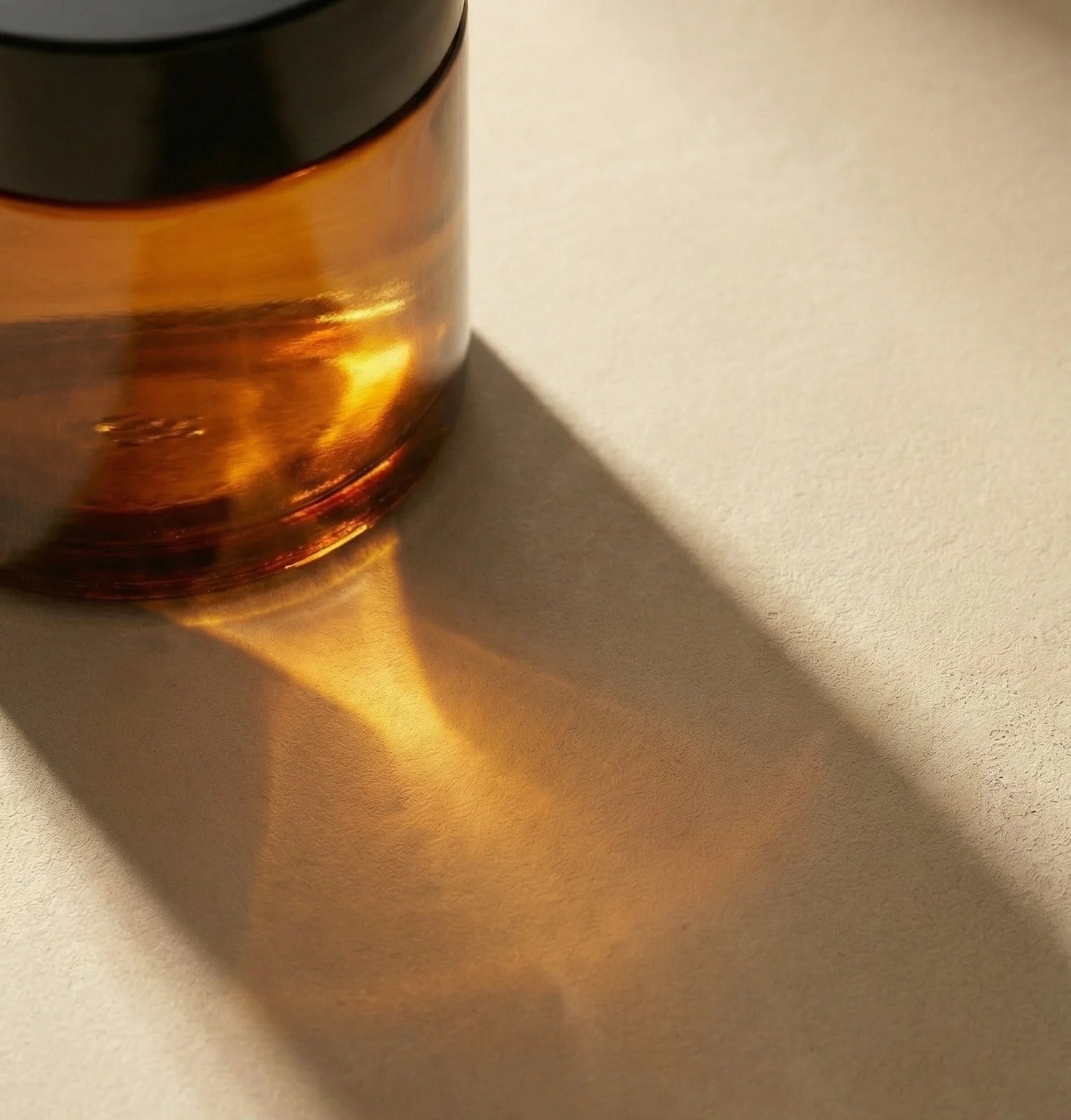 Amber glass Faeora jar with a black lid on a beige surface.